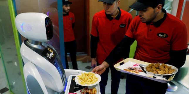 A waiter places plates with food onto the tray of a waitress robot (Timea) at the Times Fast Food restaurant in Kabul